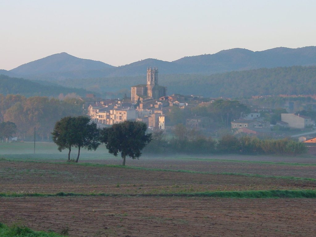 Imatge panoràmica del nucli de La Pera amb les Gavarres al fons. Del nucli en destaca l'església de Sant Isidor, construït entre els segles XVI-XVIII en un estil gòtic-renaixentista sobre del temple antic del segle X.