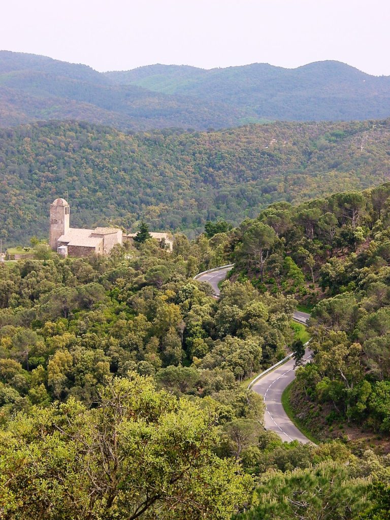 Imatge distant del conjunt de Santa Pellaia, format per l'església, la rectoria i dos masos; enmig de la immensitat de les Gavarres. De l'església en destaca la torre campanar de planta quadrada coronat amb cúpula.