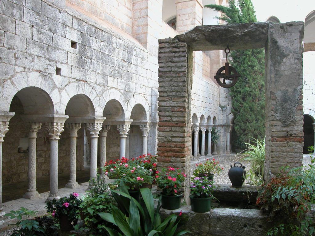 A l'entrada de Girona a les Gavarres trobem un dels monestirs benedictincs més antics de Catalunya. La imatge ens mostra el claustre del cenobi, amb la seva doble arcuació de columnes amb els capitells amb motius vegetals. En el primer terme hi ha el pou d'aigua amb la politja i un càntir.