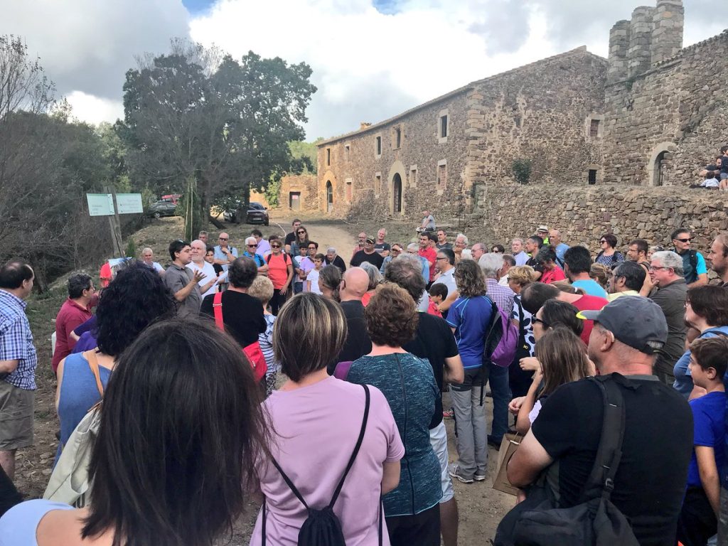 Instant de l'aplec on Elvis Mallorquí fa una explicació de can Darna i la família de masovers que hi va viure els últims anys. Es veu el conjunt arquitectònic de la rectoria, el castell i l'església al fons.